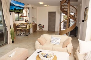 A modern living room with a sofa, a dining area, a TV, and a spiral staircase. - Villa Sunset Lagonisi (Saronikos)