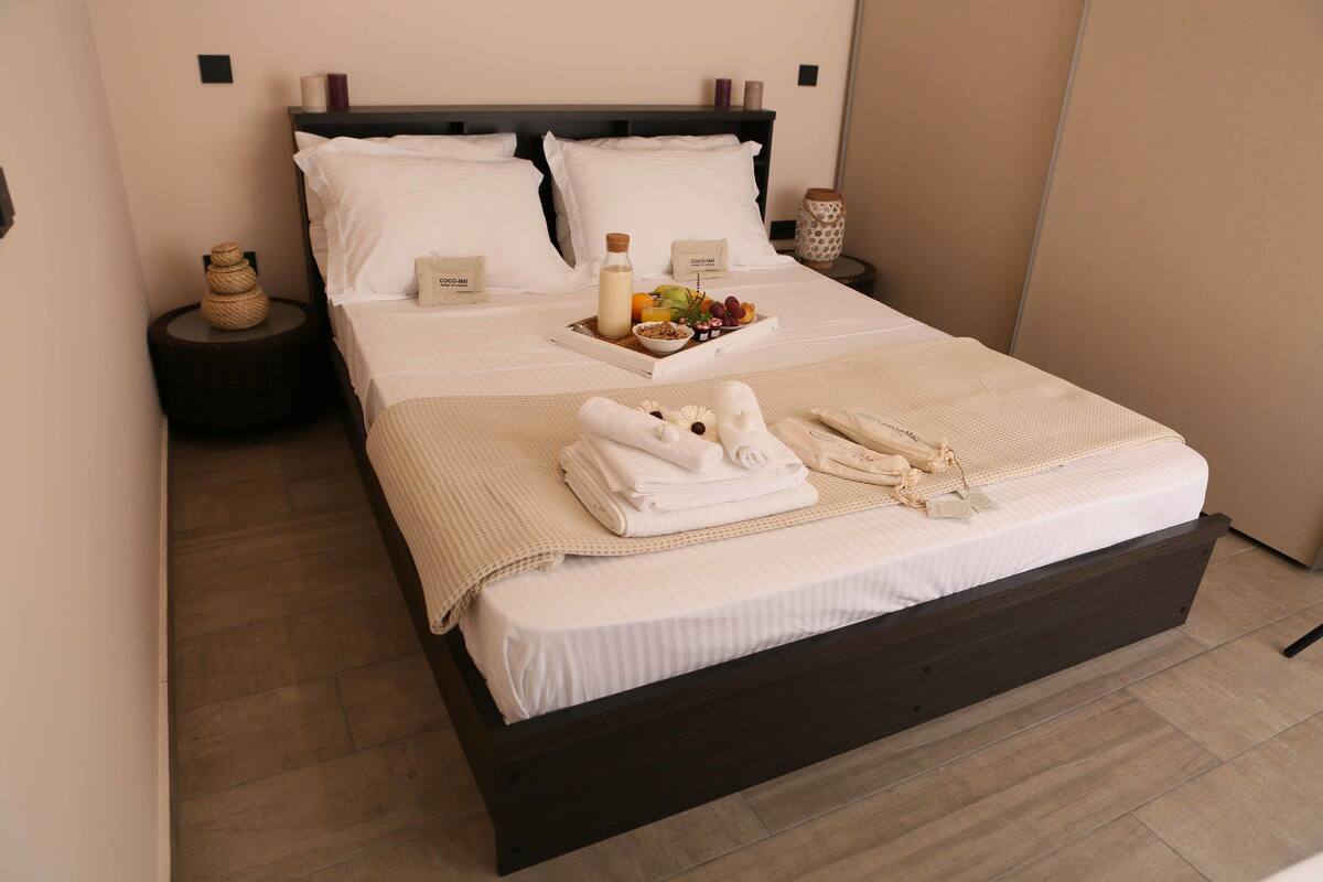 A neatly made bed with a tray of breakfast items, towels, and a bottle of milk on the nightstand.