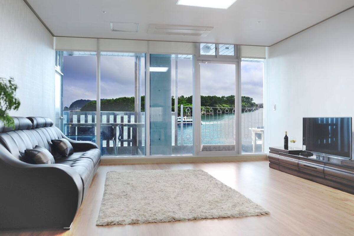 A modern living room with a large sliding glass door leading to a balcony with a view of a body of water and hills.