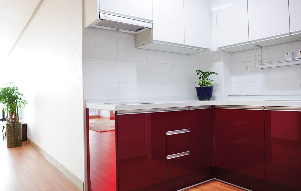 A modern kitchen with white cabinets, a red countertop, and a potted plant.