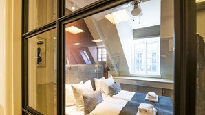 Une chambre d’hôtel avec une grande fenêtre, un lit avec du linge de lit blanc et une vue sur le paysage urbain.