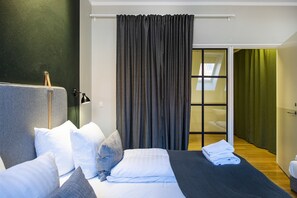 Ein modernes Schlafzimmer mit einem großen Bett, grauen Vorhängen und Blick auf einen Balkon.