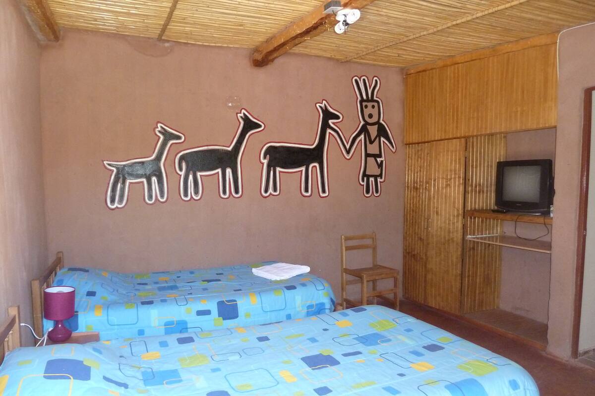 Quarto com duas camas, televisão e uma parede com desenhos de animais.