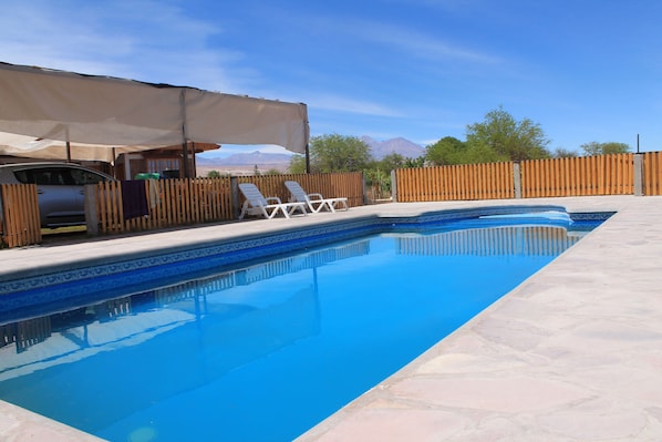 A swimming pool with a wooden fence, lounge chairs, and a car parked nearby.