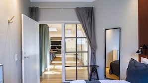 Ett hotellrum med en säng, en spegel, ett nattduksbord och utsikt över hallen och köksdelen.