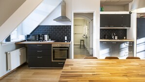 Ett modernt kök med en svart tegelvägg bakom arbetsbänken, träbänkskivor och en inbyggd ugn. Det finns också en matplats med ett träbord och stolar.