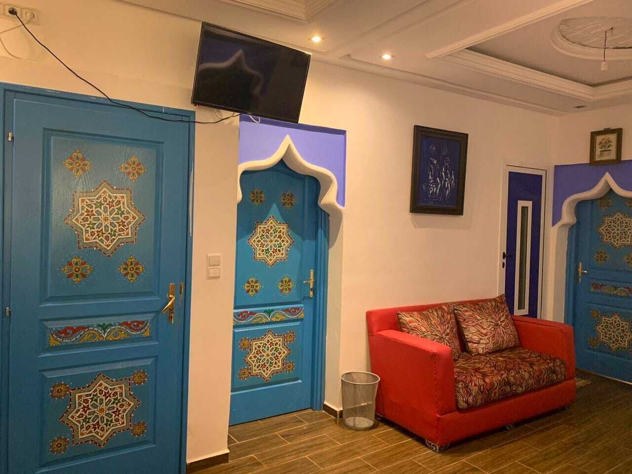 A room with two blue doors with intricate designs, a red sofa, and a television mounted on the wall.