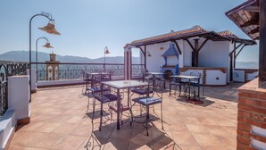 A terrace with outdoor seating, a view of the sea, and a building with a tiled roof. - Dar Saida Hora (Chefchaouen)