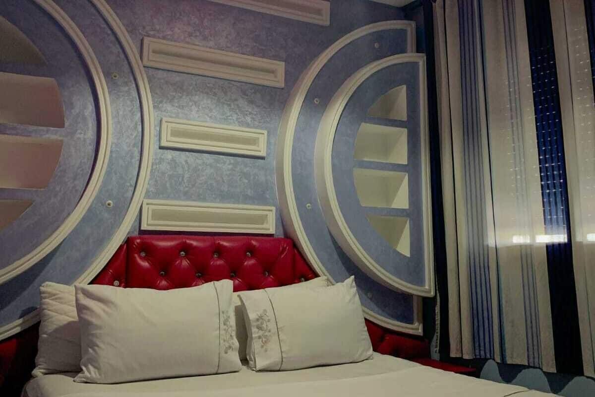 A bedroom with a red tufted headboard, a large bed, and a circular ceiling light.