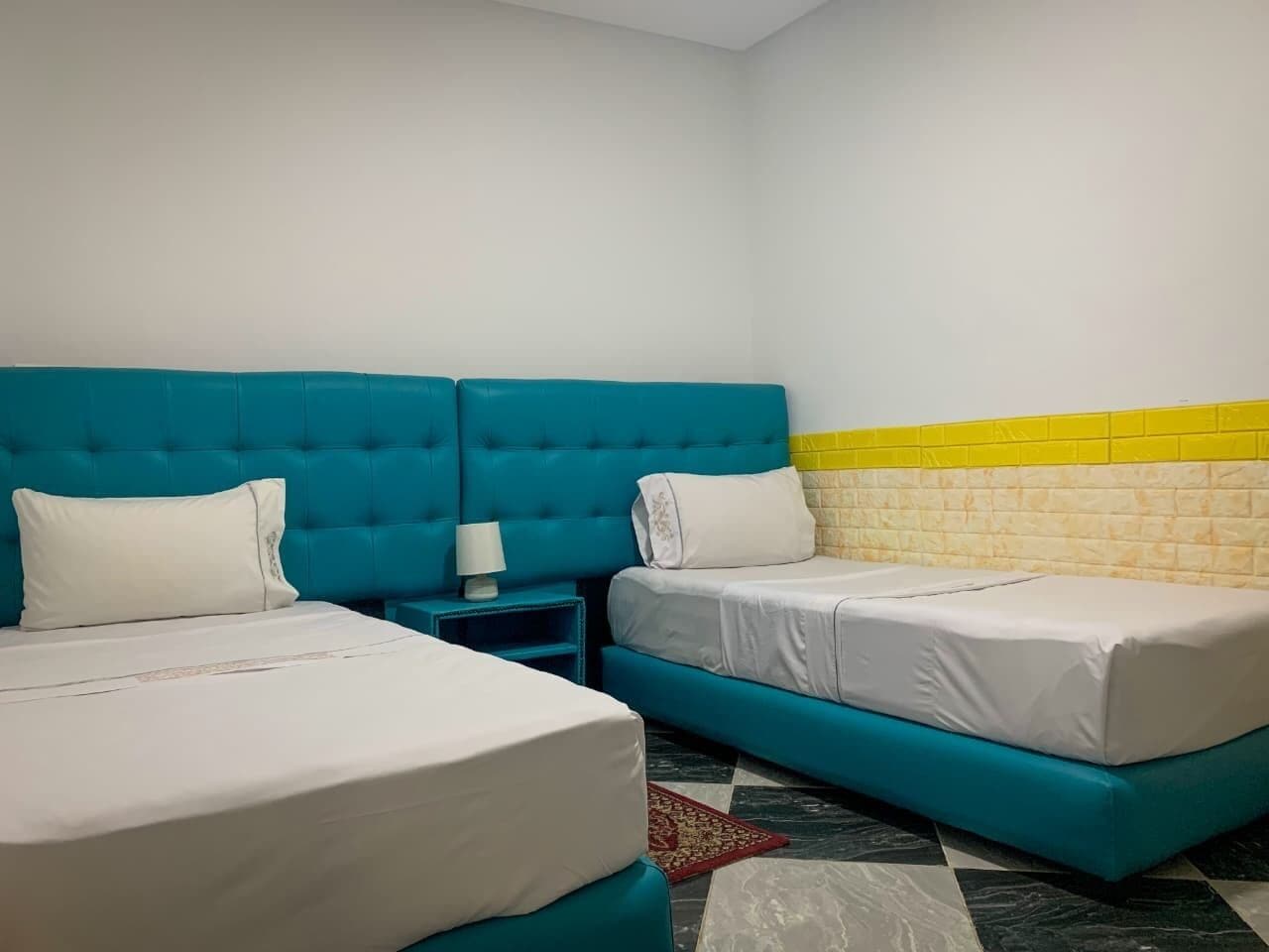 A room with two beds, a nightstand, and a tiled wall.
