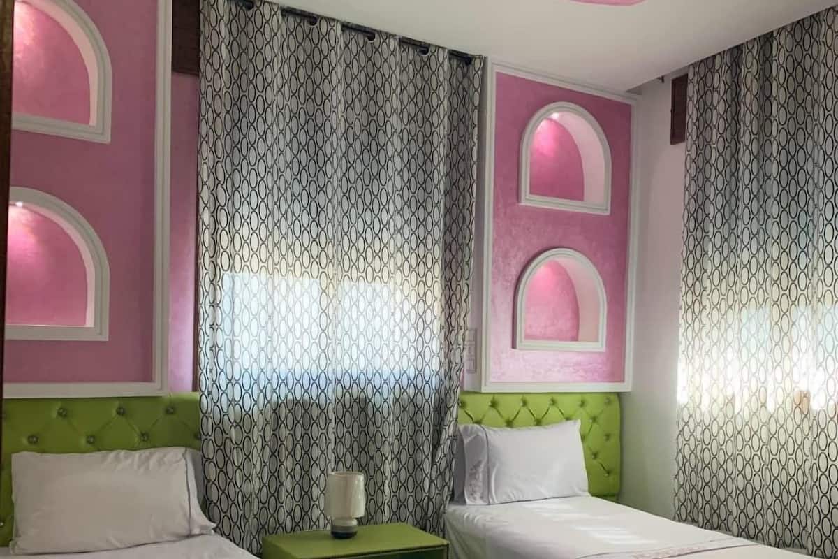 A bedroom with two beds, a green nightstand, a patterned curtain, and a ceiling with a pink design.