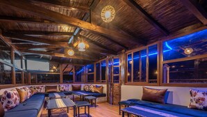 A cozy, rustic room with wooden beams, large windows, and a mix of seating options including sofas and tables. - Dar Saida Hora (Chefchaouen)
