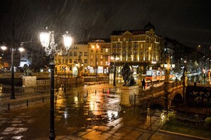 Una plaza urbana iluminada de noche con una estatua, un puente y edificios.