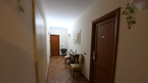 Un pasillo con puerta de madera, una pequeña mesa con silla y un aplique en la pared.
