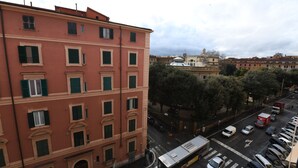 Un edificio de varios pisos con fachada roja y contraventanas verdes, mostrando una vista de la calle con automóviles estacionados y un autobús.