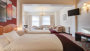 A hotel room with two beds, a sitting area with a table and chairs, a TV mounted on the wall, and a chandelier. - Hotel Consul (Kiel)