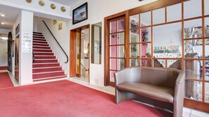 A hotel lobby with a red carpet, a staircase, a brown leather sofa, and large windows with frosted glass panels. - Hotel Consul (Kiel)