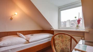 A small, cozy room with a single bed, a chair, a table, and a window with a view of buildings.