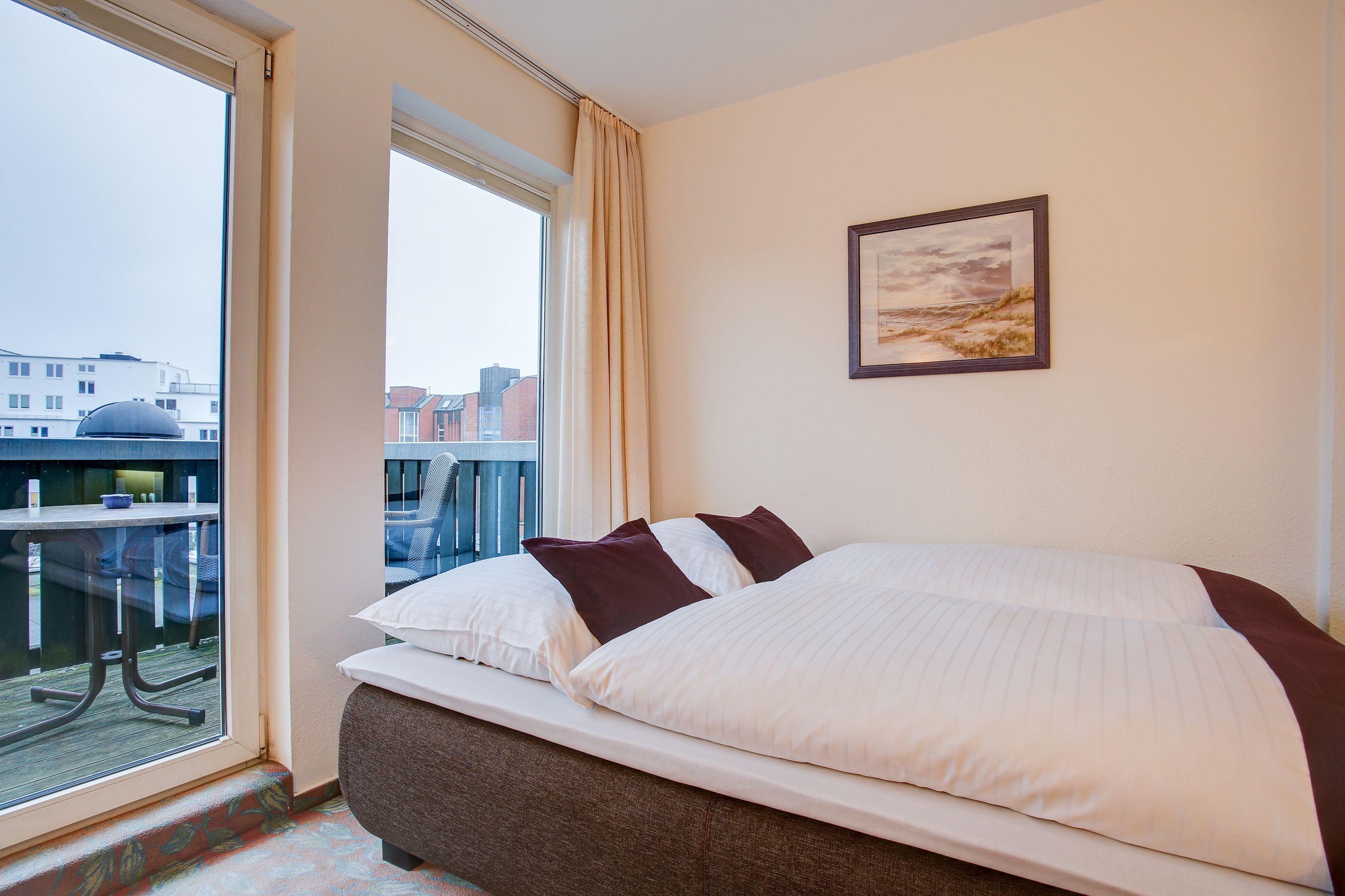 A hotel room with a large bed, a window with a view of the city, and a painting on the wall.