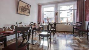 A dining area with wooden flooring, multiple tables and chairs, and a large window with curtains. - Hotel Consul (Kiel)