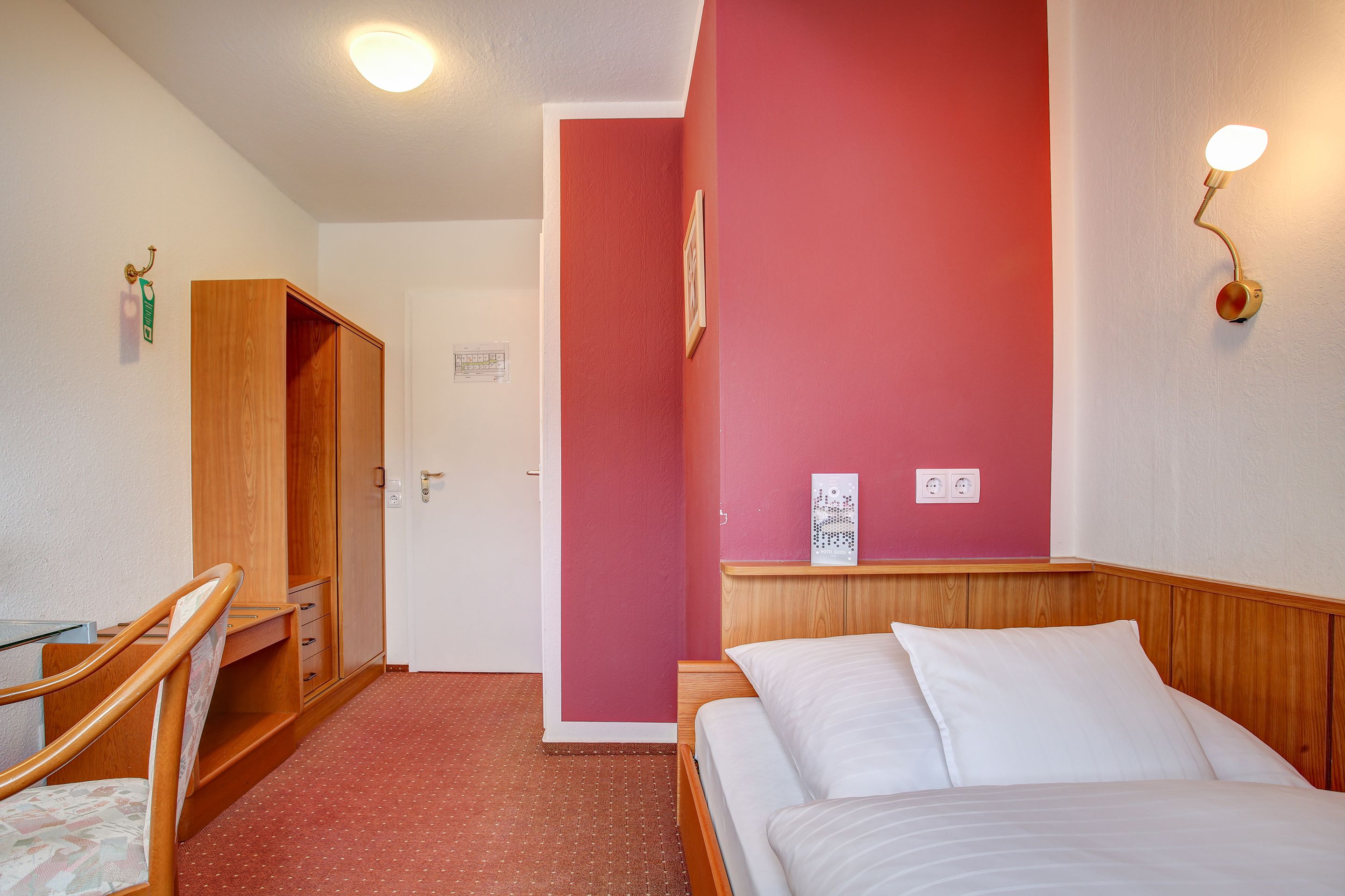 A hotel room with a bed, a desk, and a wardrobe.