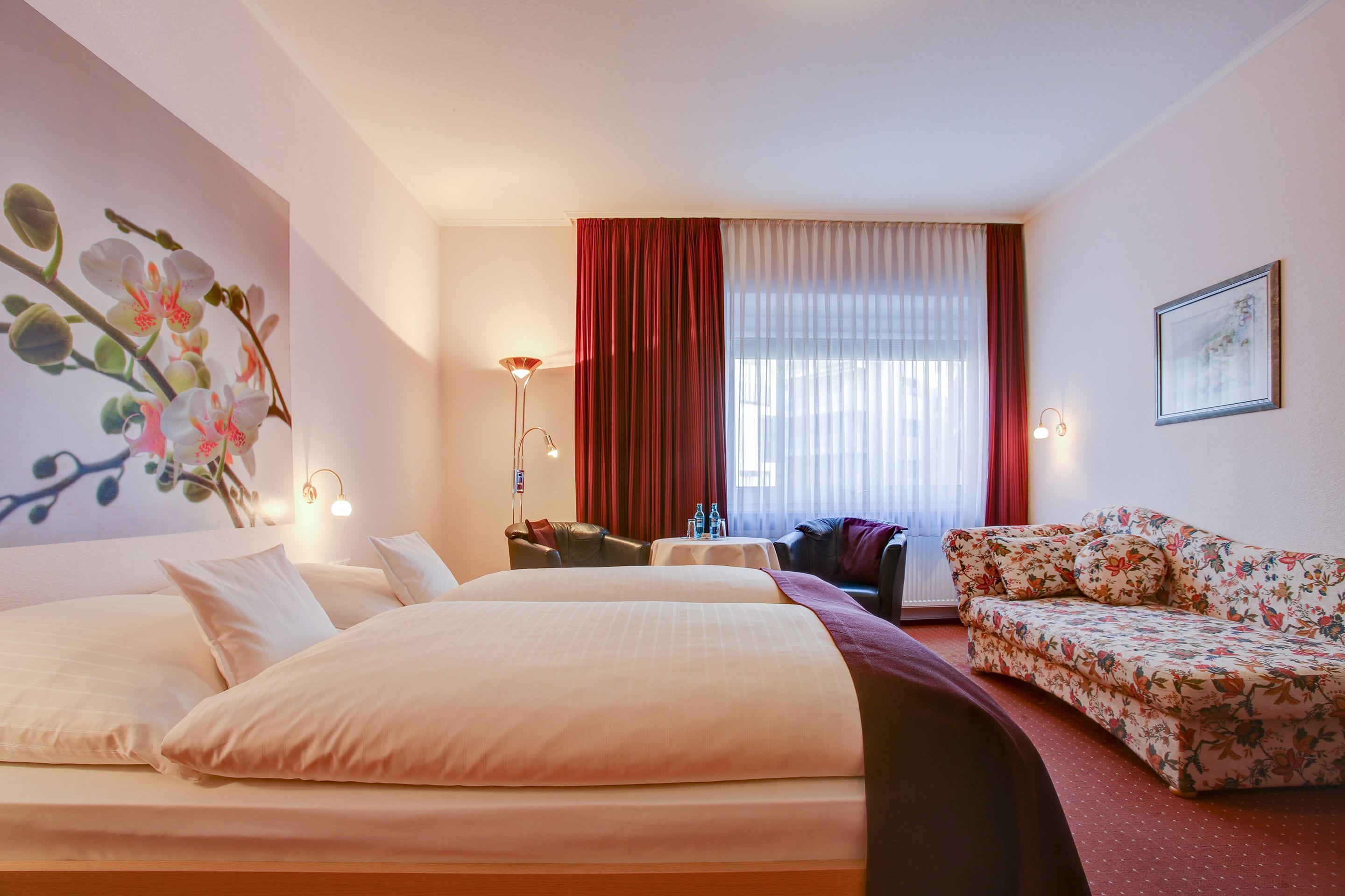 A hotel room with a large bed, a sofa, a desk, and a window with curtains.