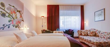 A hotel room with a large bed, a sofa, a desk, and a window with curtains.