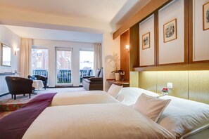 A hotel room with two beds, a desk, a chair, and a balcony with a view of buildings. - Hotel Consul (Kiel)