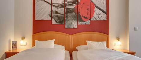 Habitación de hotel con una cama grande, dos mesitas de noche y una obra de arte de una rosa colgada en la pared.
