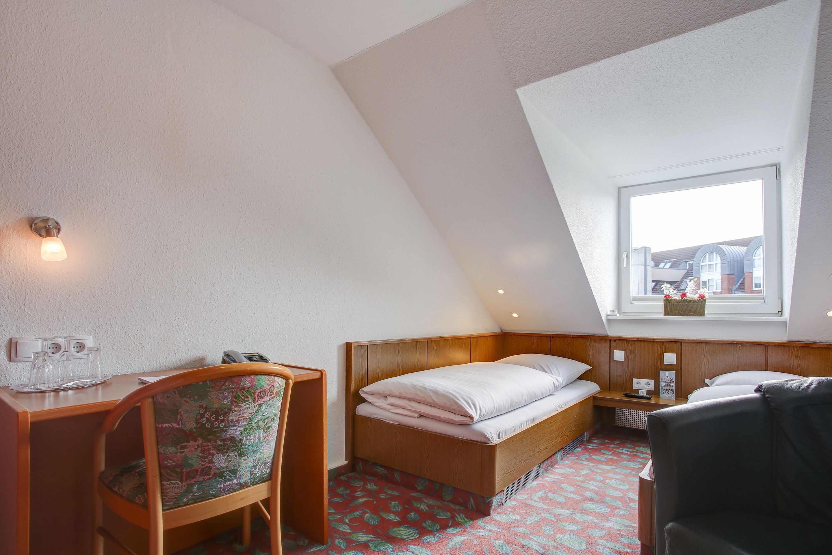Una habitación pequeña y acogedora con una cama de madera, un escritorio con silla y una ventana con vistas a edificios.