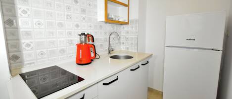Una cocina con gabinetes blancos, un lavamanos, una encimera, una cafetera y un refrigerador blanco.