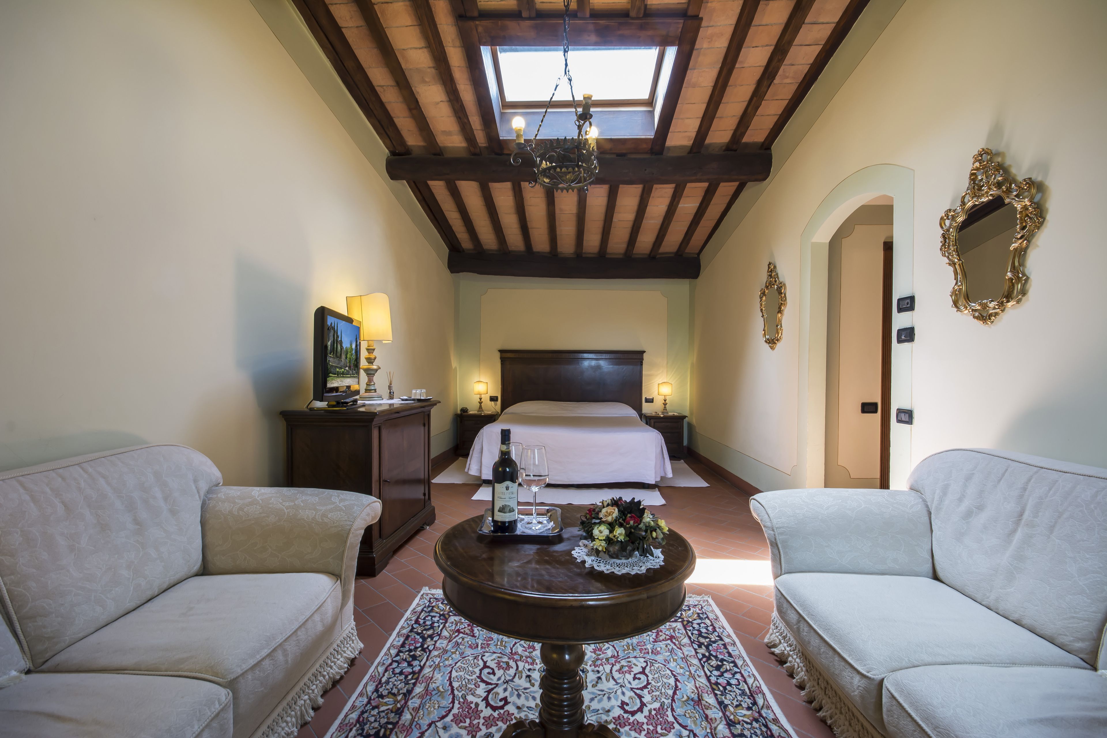 Una habitación de hotel con una cama, dos sofás, una mesita con una botella y vasos, y un candelabro.