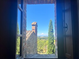 Un umbral abierto que da a la vista de un edificio histórico con tejado de tejas y chimenea, rodeado de vegetación y un cielo azul despejado.