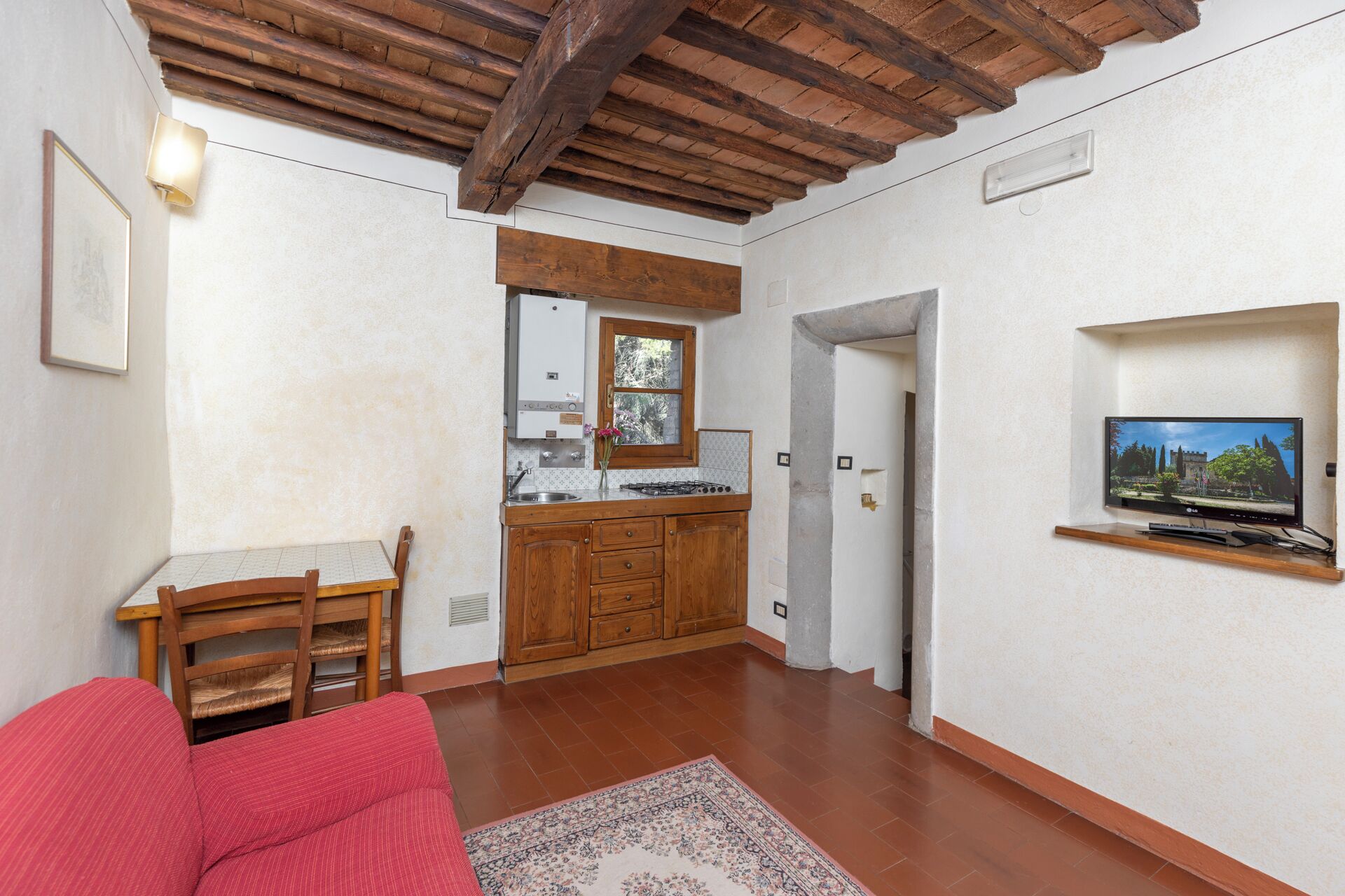 Un espacio habitable compacto con kitchenette, zona de comedor y televisor montado en la pared.