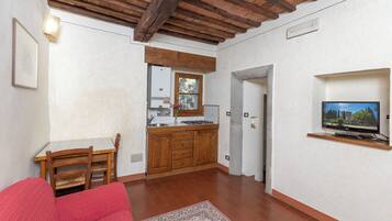 Un espacio habitable compacto con kitchenette, zona de comedor y televisor montado en la pared.