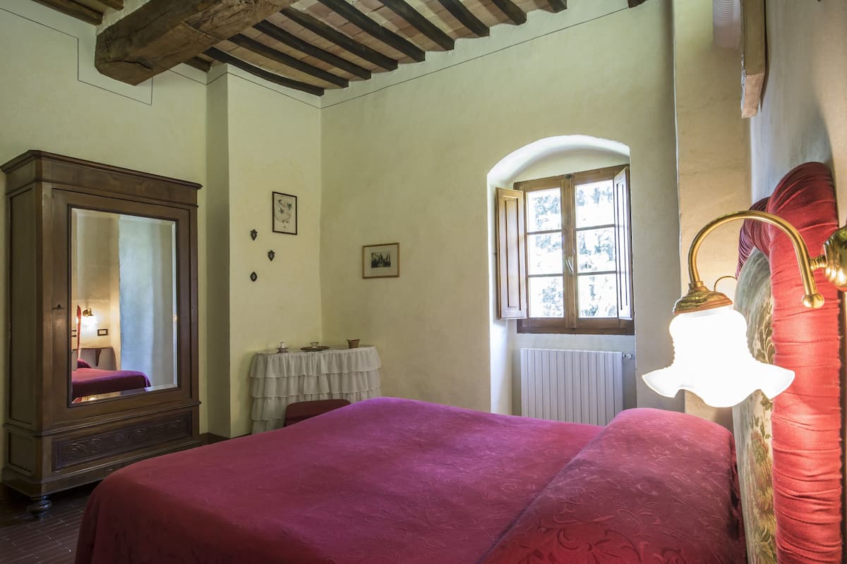 Un dormitorio con cama, espejo, ventana y lámpara.