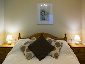 A neatly made bed with a pillow, two bedside lamps, a nightstand, and a framed picture on the wall.