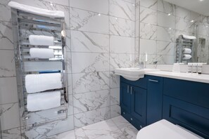 A modern bathroom with marble tiles, a glass towel rack, a sink, and blue cabinets.