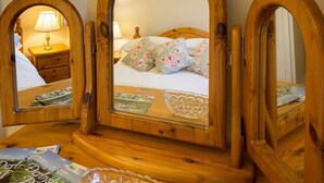 A wooden vanity with three mirrors, a bed with floral bedding, a nightstand with a lamp, and a framed picture on the wall. - The Barrel Inn (Hope Valley)