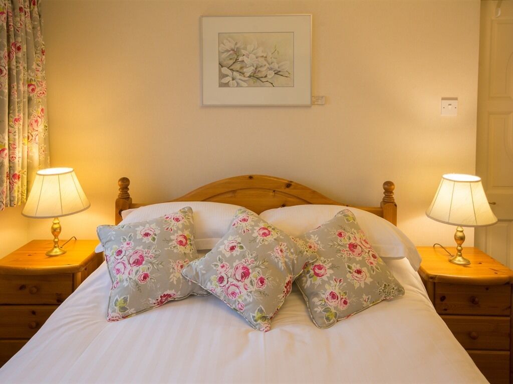 A neatly made bed with floral pillows, two bedside lamps, and a framed artwork on the wall.