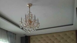 Un dormitorio con un cabecero capitonado, una cama grande con ropa de cama floral, un banco al pie de la cama y una araña.