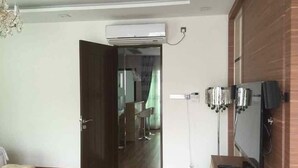 Una habitación con piso de madera, una cama, un televisor montado en la pared y un equipo de aire acondicionado.