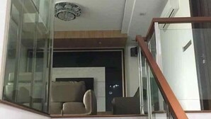 Una escalera con peldaños de madera y barandilla de cristal que conduce a una sala de estar con sofá y mesa de centro.