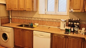 A kitchen with wooden cabinets, a washing machine, a dishwasher, a sink, and a window with blinds. - Apartment near Fountain Square (Baku)