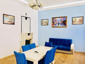 A room with a white table, blue chairs, a blue sofa, and four framed paintings on the walls. - Apartment near Fountain Square (Baku)