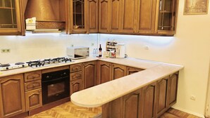 A kitchen with wooden cabinets, a gas stove, a microwave, and a sink. - Apartment near Fountain Square (Baku)