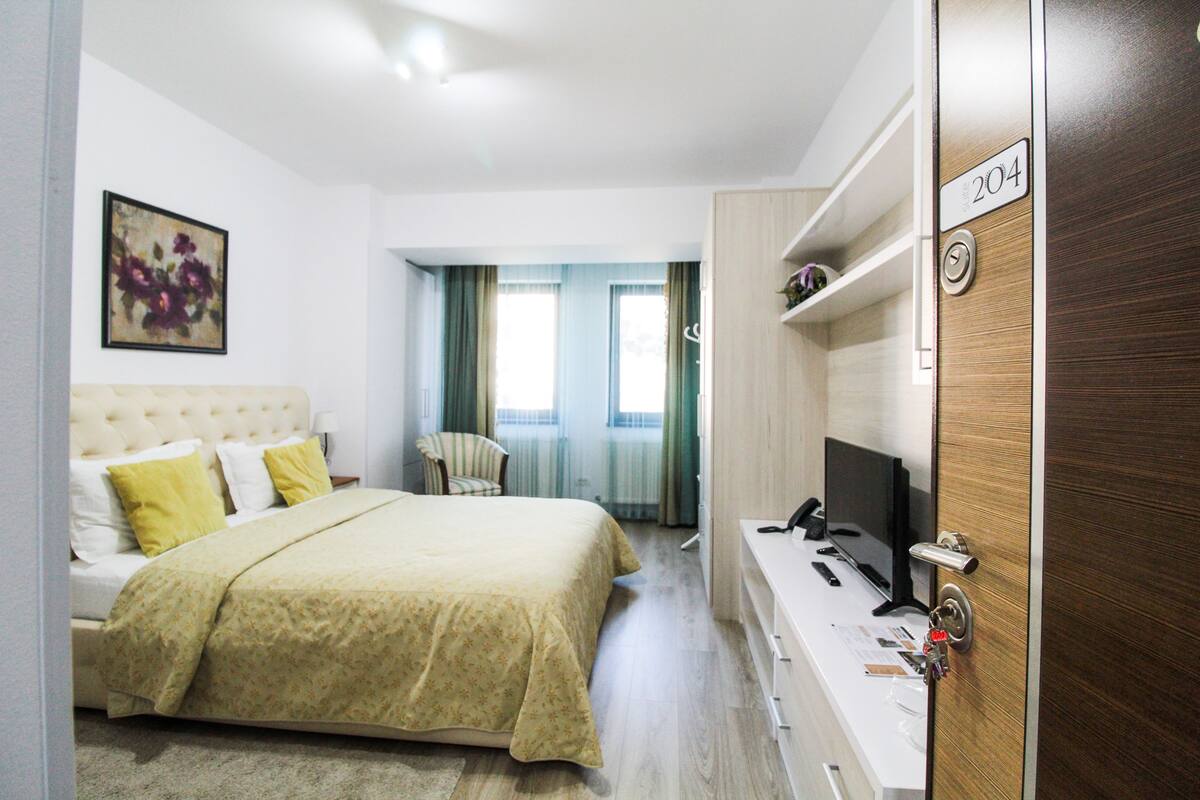 A hotel room with a bed, a desk with a computer, a chair, and a TV.