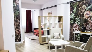 Ein modernes Wohnzimmer mit einer Couch, einem Sessel und einem Couchtisch. Im Hintergrund ist ein Bücherregal und eine rote Couch zu sehen.