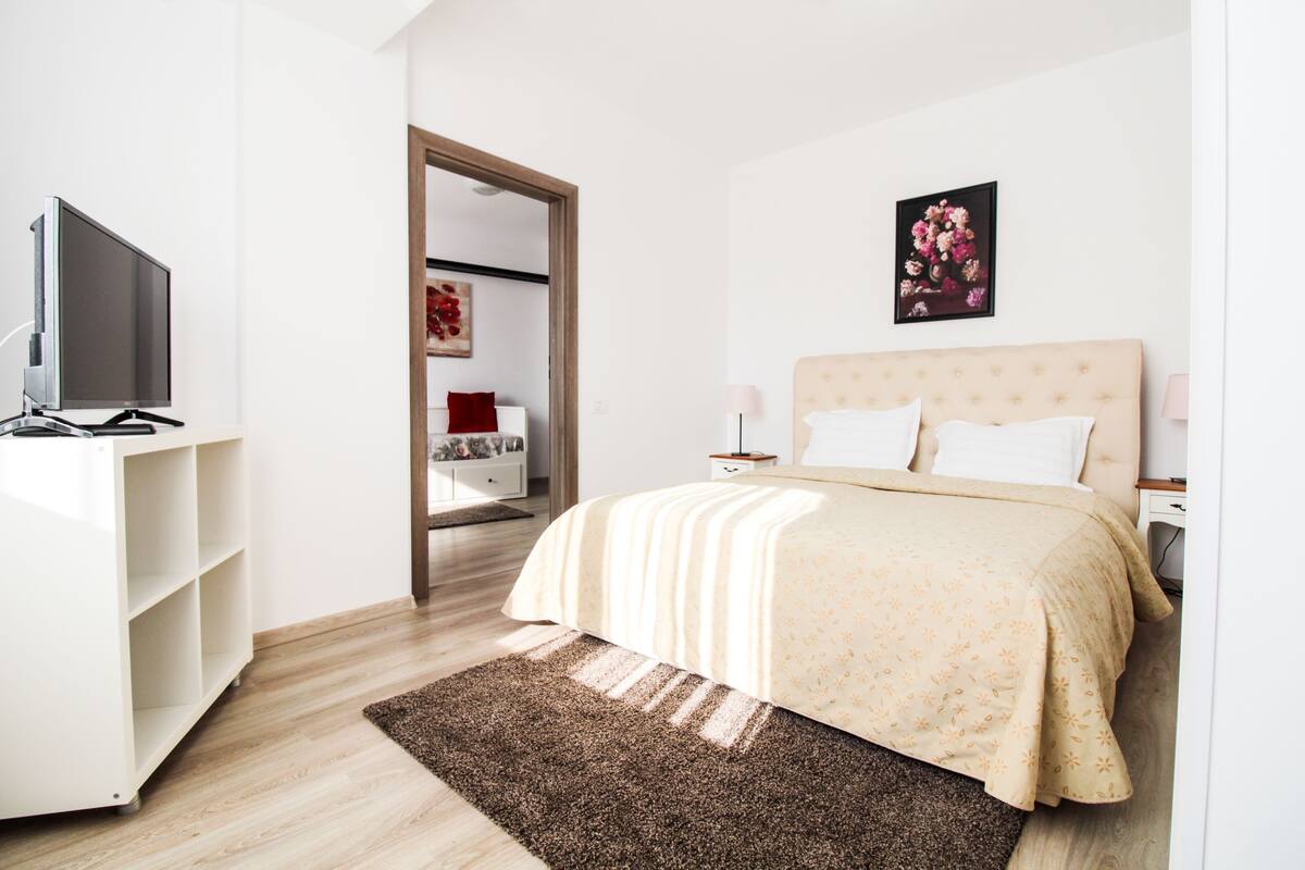 A bedroom with a bed, a TV, a wardrobe, and a painting on the wall.