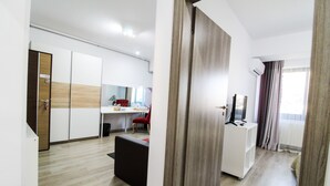Ein modernes Hotelzimmer mit Holzboden, einem weißen Schrank, einem roten Sessel und einem Fernseher auf einem weißen Lowboard.